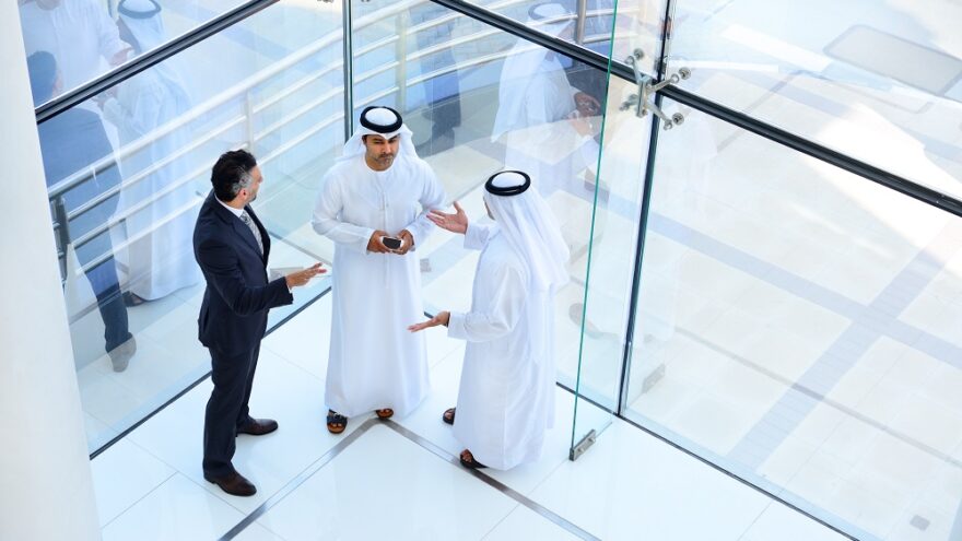 Three middle eastern business people having a conversation in a modern glass office.