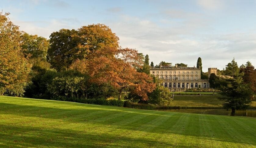 A large mansion behind a field and trees