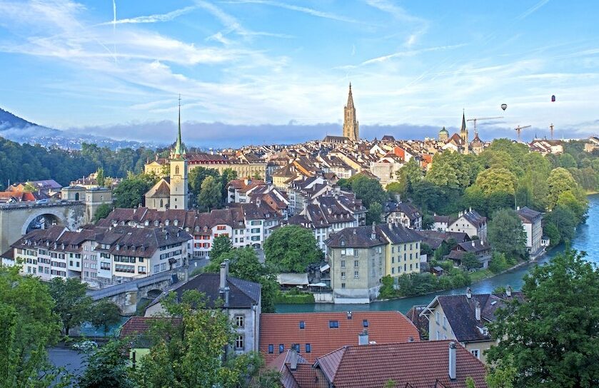 skyline of Bern, Switzerland with houses in front and lots of blue sky containing two hot air balloons