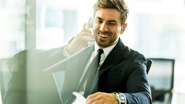 A high-profile personal assistant in a business suit taking a call at his desk.