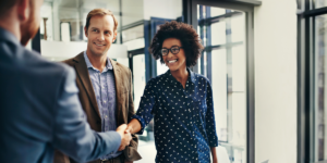 Three business people dressed in professional wear, two of them are shaking hands and smiling