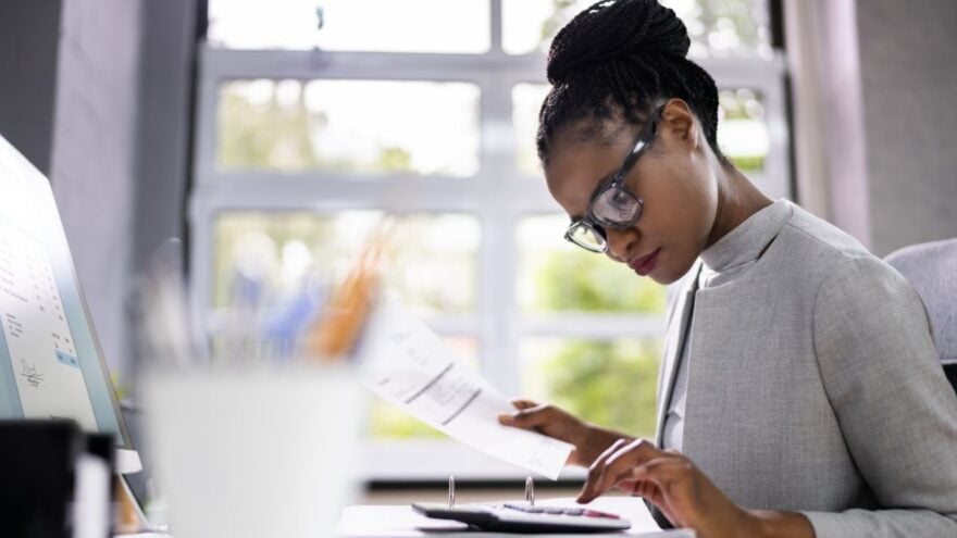 Woman sat at her desk wearing glasses, typing on a calculator