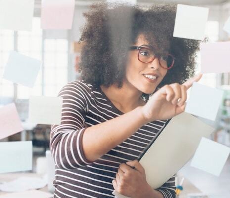 A business woman holding a file, pointing at a screen.