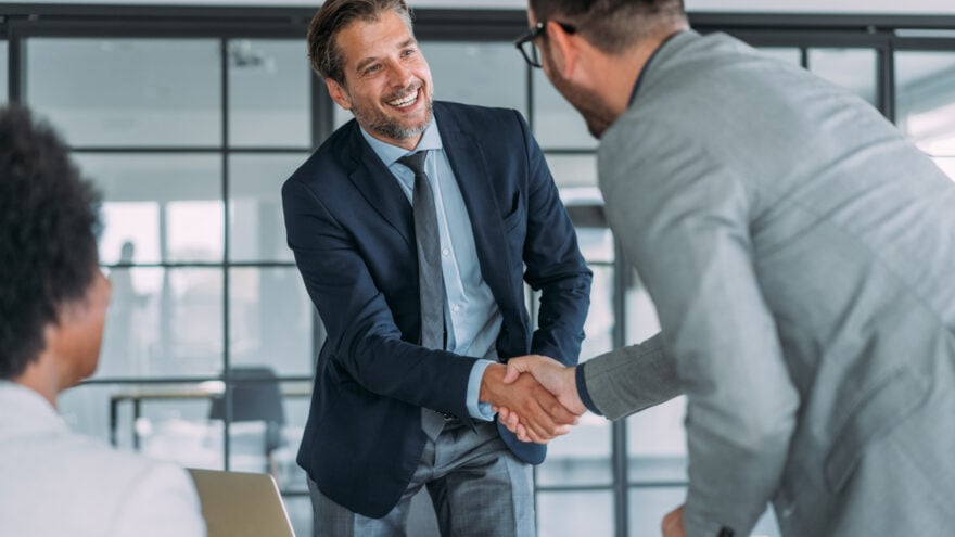 Business people handshaking across the table during a meeting in modern office. Group of business persons in business meeting. Three entrepreneurs on meeting in board room. Corporate business team on meeting in the office.