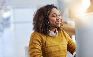 woman in yellow sweater behind computer with headphones in