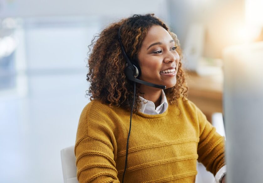 woman in yellow sweater behind computer with headphones in