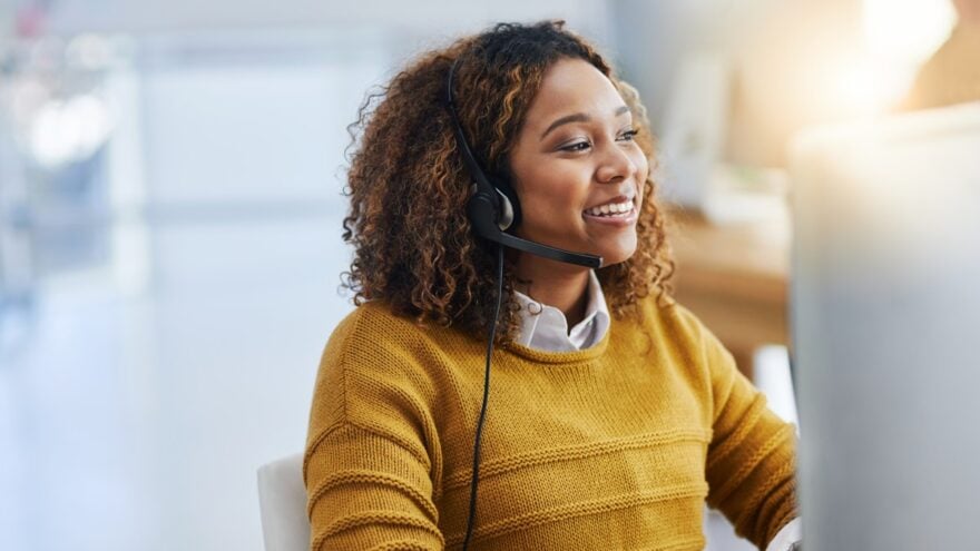 woman in yellow sweater behind computer with headphones in
