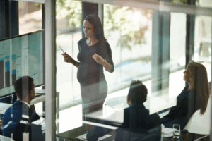 A pregnant person giving a presentation to their colleagues in a bright, modern office.