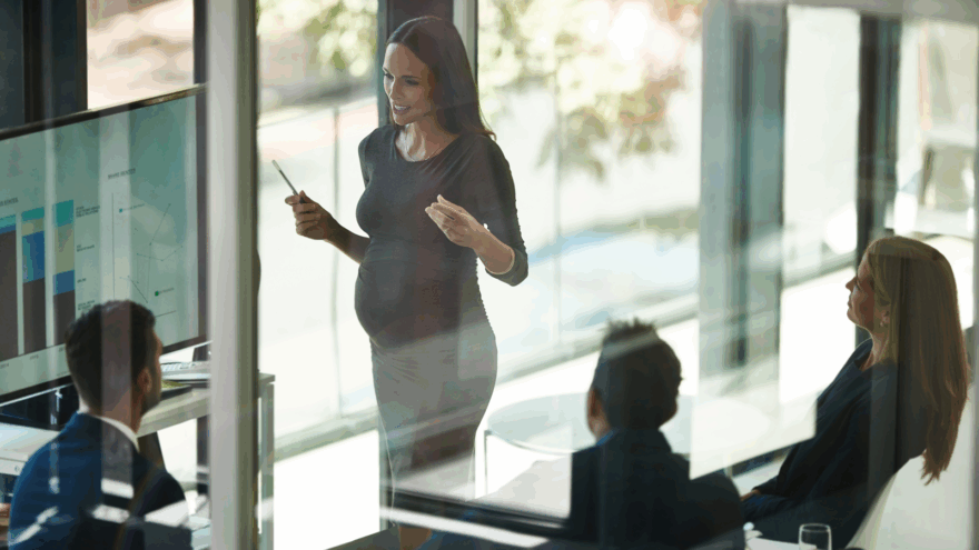 A pregnant person giving a presentation to their colleagues in a bright, modern office.