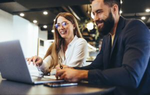 Woman and man in the office, smiling while working on a laptop.