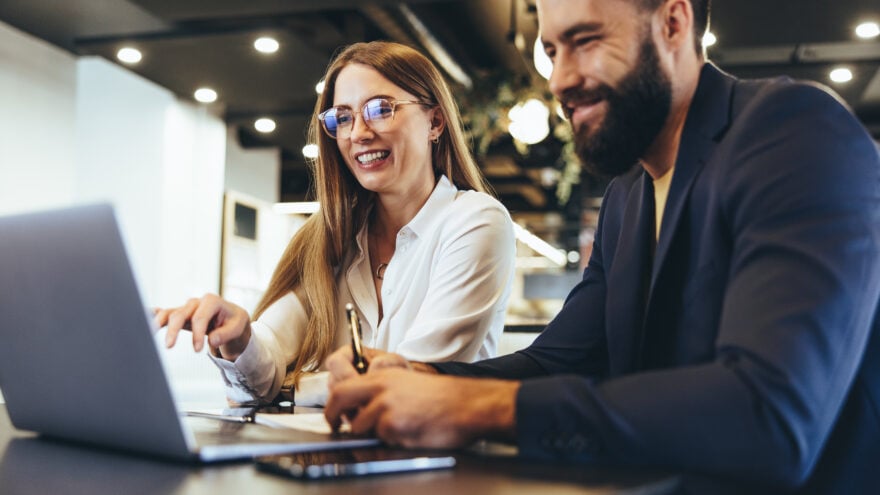 Woman and man in the office, smiling while working on a laptop.