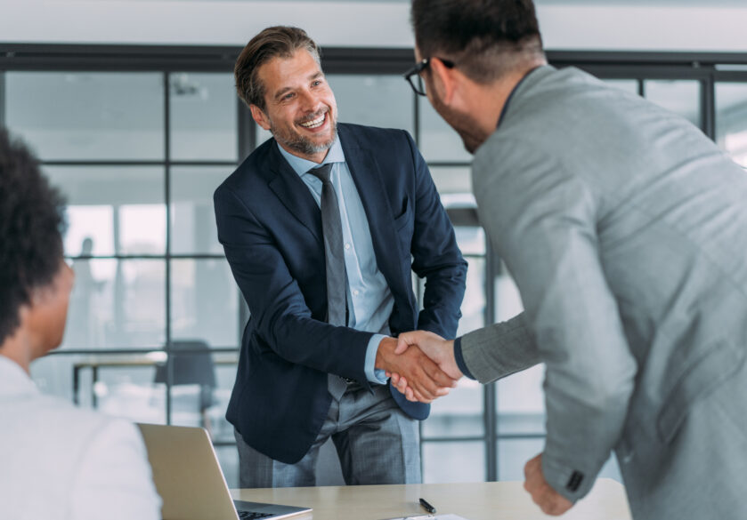 Business people handshaking across the table during a meeting in modern office. Group of business persons in business meeting. Three entrepreneurs on meeting in board room. Corporate business team on meeting in the office.